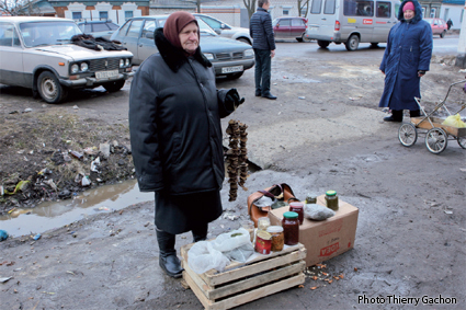 Photo d'une personne agée vendant des champignons et des confitures sur un marché.
